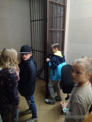 zdjęcie przedstawia fragment pomieszczenia dla osób zatrzymanych oraz czwórkę dzieci zwiedzających je