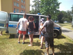 Zdjęcie wykonane jest w plenerze, znajduję się na nim bus policyjny przed którym stoją dorośli i dzieci, którzy chcą go obejrzeć
