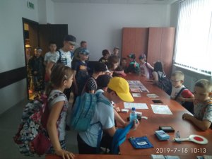 zdjęcie przedstawia pokój w którym znajduje się grupa dzieci, które oglądają różne przedmioty znajdujące się na biurkach, między innymi tarcze do zatrzymywania pojazdów, zdjęcia, odbitki linii papilarnych