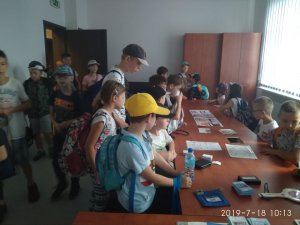zdjęcie przedstawia pokój w którym znajduje się grupa dzieci, które oglądają różne przedmioty znajdujące się na biurkach, między innymi tarcze do zatrzymywania pojazdów, zdjęcia, odbitki linii papilarnych