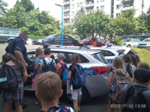 zdjęcie wykonane jest na parkingu, widać na nim radiowóz, policjanta oraz grupkę dzieci oglądających samochód