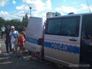 na zdjęciu znajduje się radiowóz policyjny, policjantka i dzieci, które oglądają samochód