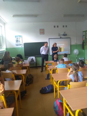 zdjęcie przedstawia salę lekcyjną, w której znajduje się policjantka i pracownik biura bezpieczeństwa i zarządzania kryzysowego, dzieci siedzą w ławkach i słuchają prelekcji