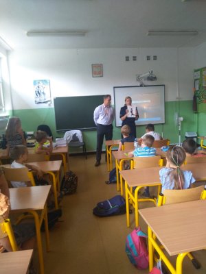 zdjęcie przedstawia salę lekcyjną, w której znajduje się policjantka i pracownik biura bezpieczeństwa i zarządzania kryzysowego, dzieci siedzą w ławkach i słuchają prelekcji