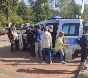 Policjantka prezentuje radiowóz i sprzęt policyjny dzieciom, podczas pikniku.